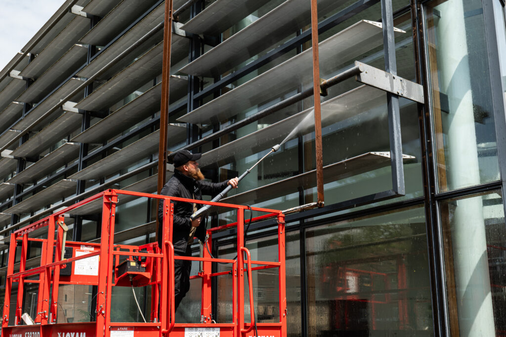 Medarbejder fra TM Boligservice pudser en glasfacade fra en lift